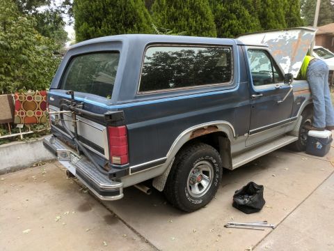 1996 Ford Bronco - A person works on the engine of a 1996 Ford Bronco parked on a driveway.