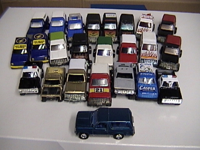 Collection of toy trucks on a white table with a blue toy Bronco SUV in front