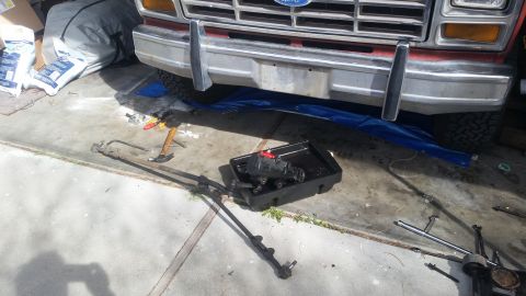 1985 Ford Bronco - Front end of a Ford truck with steering parts laid out on the ground for repair.