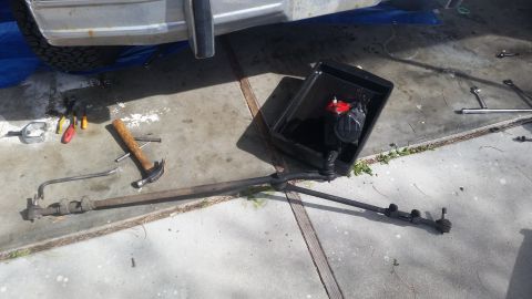 1985 Ford Bronco - Tools and a disassembled steering linkage are on the ground next to a vehicle undergoing maintenance.