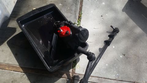 1985 Ford Bronco - Steering gearbox and tie rod assembly are shown in a drain pan, likely after removal from a vehicle.