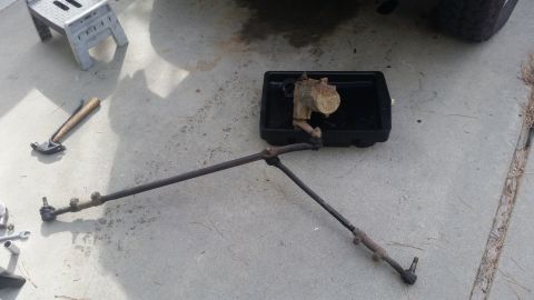 1985 Ford Bronco - Steering linkage components laid out on concrete, with tools and a drip pan. The registry claims this is from a 1985 Ford Bronco.