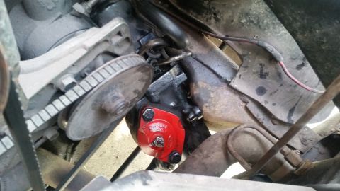 1985 Ford Bronco - Close-up view of a red painted engine component with visible bolts, situated near a pulley and belt system.