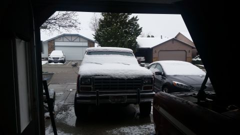 1985 Ford Bronco - Two vehicles sit parked outside in the snow, with one appearing to be an older model SUV.