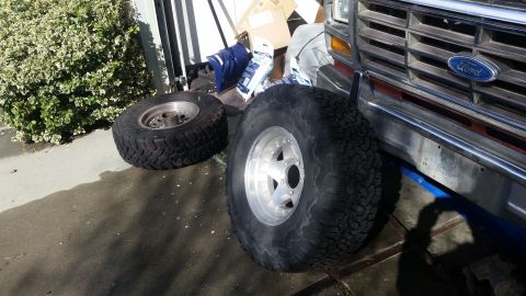 1985 Ford Bronco - Ford Bronco front end with two off-road tires staged nearby.