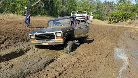 1988 Ford Bronco - A muddy Ford Bronco navigates a challenging off-road course, with other vehicles visible in the background.