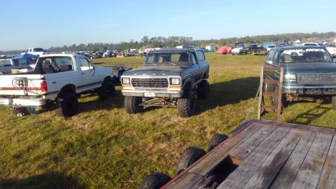 1988 Ford Bronco - A lifted Ford Bronco sits in a grassy field with other vehicles and tents in the background.