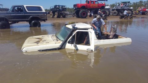 1988 Ford Bronco - A white pickup truck, likely from the 1980s, is partially submerged in mud at a mud park event.