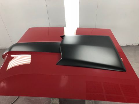 1968 Mercury Cougar - A matte black hood scoop is positioned on a red car hood, likely in a paint booth.