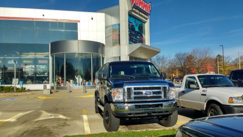 1996 Ford Bronco - A dark blue Ford E-Series van is parked in front of a Summit Racing store on a sunny day.