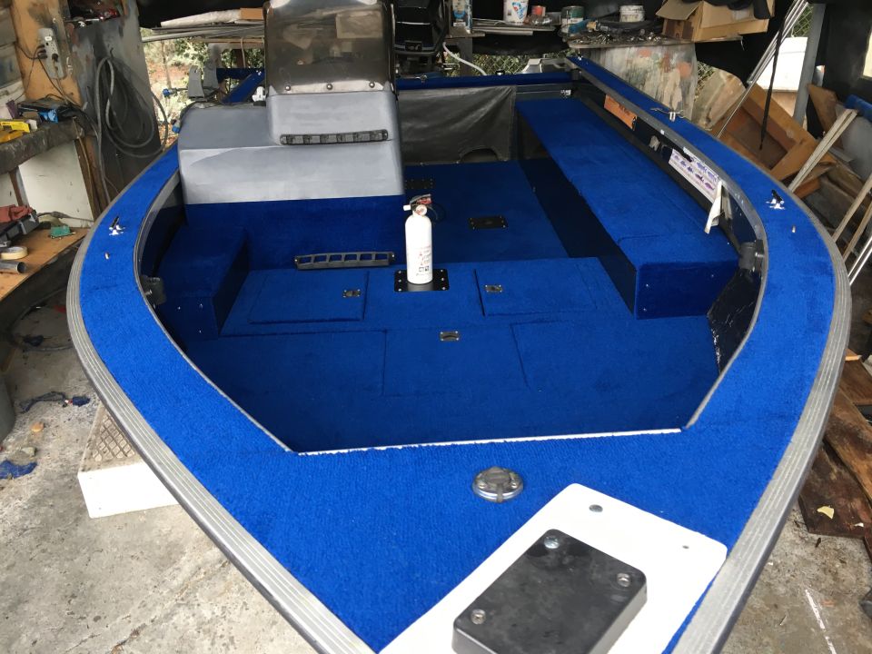 Interior of a boat with bright blue carpet, a fire extinguisher, and storage compartments
