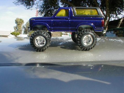 1979 Ford Bronco - blue lifted Ford Bronco die-cast scale model with oversized tires displayed on a car hood outdoors.