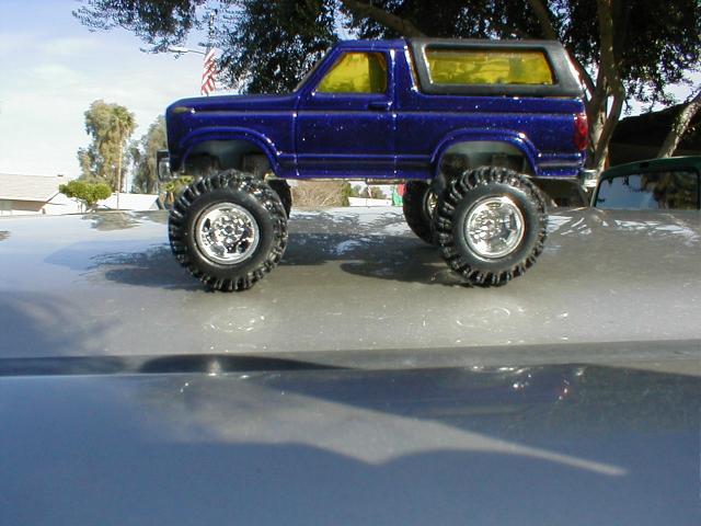 Blue lifted Ford Bronco scale model truck on car hood outdoors