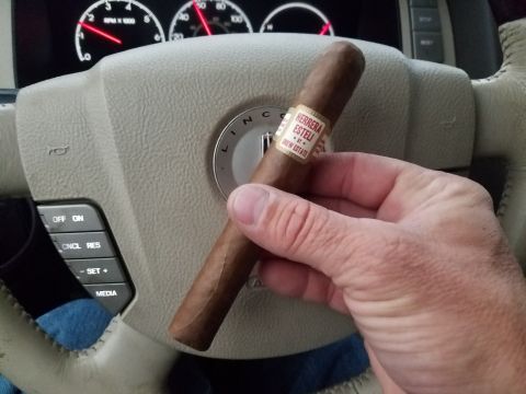 2018 Ford Bronco - A cigar is held over the steering wheel of a Lincoln, with dashboard gauges in the background.
