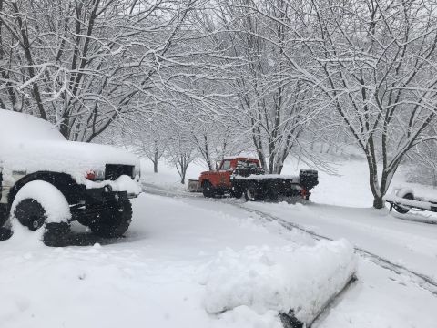 1961 Ford F-350 - An orange pickup truck equipped with a snow plow is parked in a snow-covered driveway.