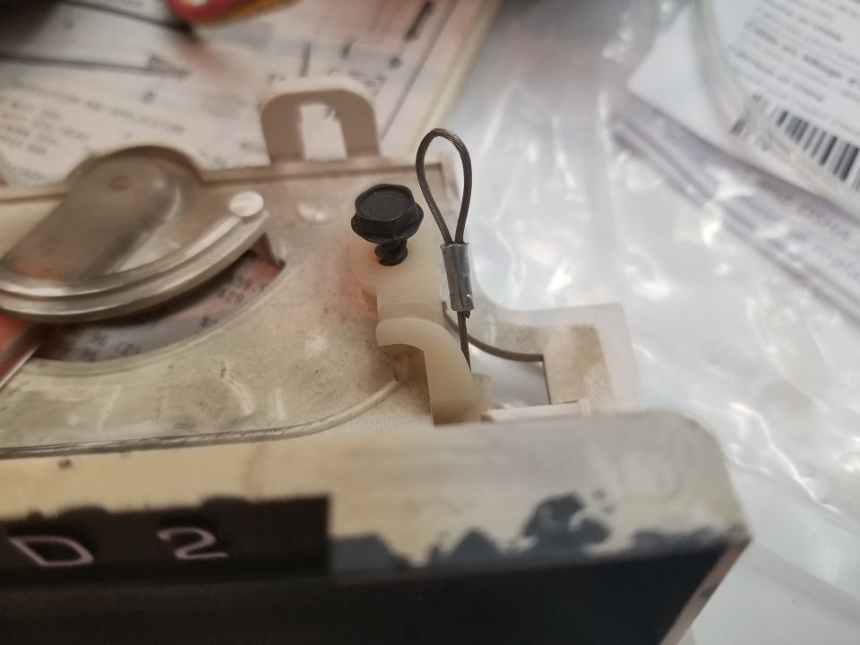 Close-up of a white plastic bracket with a black screw and wire loop attached to a beige and black component with "D 2" visible