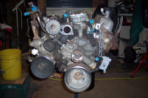1995 Ford Bronco - Engine assembly on a stand, with various components attached. A yellow bucket is visible to the left.