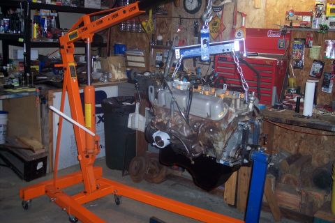 1995 Ford Bronco - An engine is being hoisted in a workshop, surrounded by various tools and storage shelves.