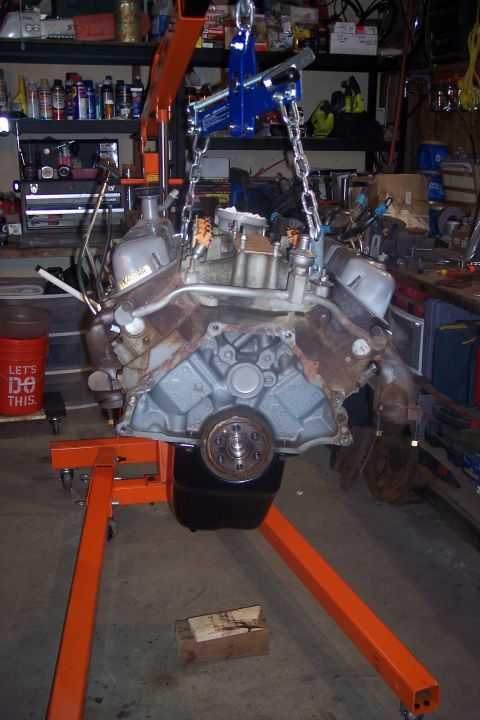 1995 Ford Bronco - Engine removed from vehicle and suspended by an engine hoist, with a red bucket nearby.