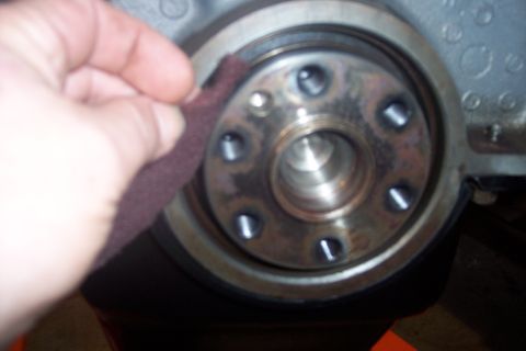 1995 Ford Bronco - A hand uses sandpaper to clean a metal engine part with visible bolts.