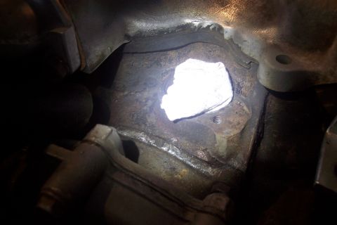1995 Ford Bronco - A close-up view of a metal engine part, possibly a gasket or intake manifold, with a white material covering an opening.