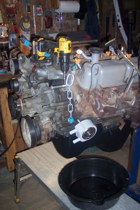 1995 Ford Bronco - Engine assembly with a drill attached via a chain, positioned over an oil pan on a workbench.