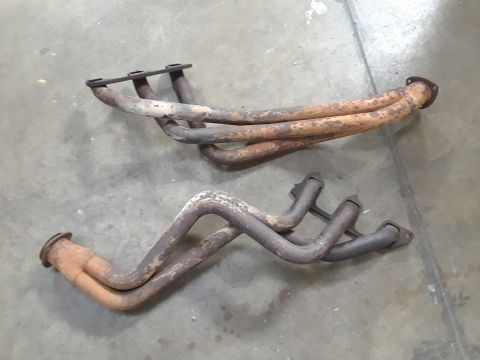 1985 Ford Bronco - Two rusty exhaust manifolds are shown on a concrete floor, likely for an engine rebuild.