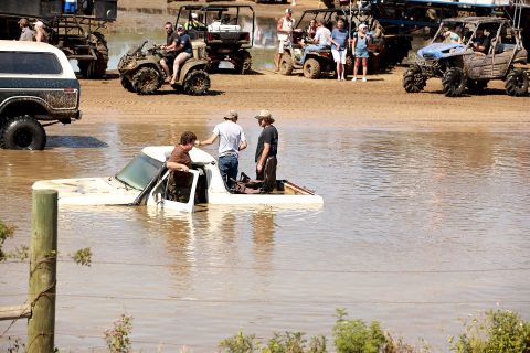 1988 Ford Bronco - People gather around a white pickup truck stuck in water at an off-road park.