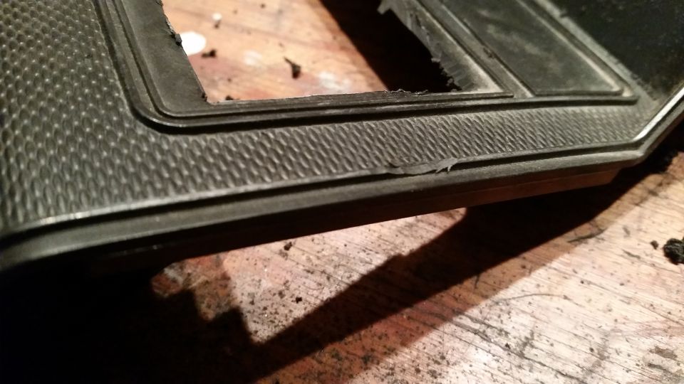 Black textured dashboard trim piece with a rectangular cutout, resting on a wooden surface