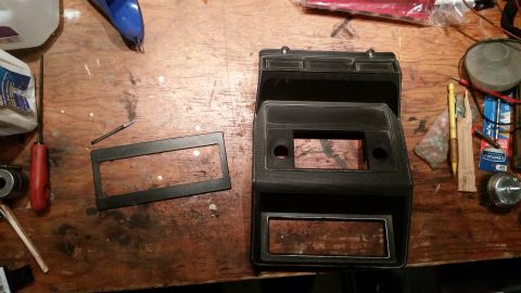 1985 Ford Bronco - Car interior parts, including a radio bezel and trim, are laid out on a workbench with various tools.
