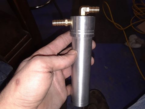 1994 Ford Bronco - A hand holds an aluminum cylindrical part with two brass hose fittings attached.