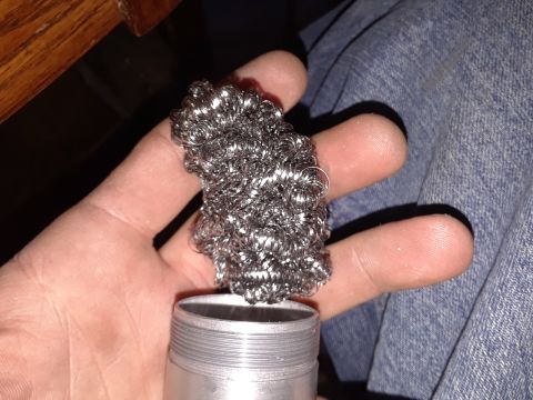 1994 Ford Bronco - A hand holds a wad of steel wool above a threaded metal cap, with a portion of blue denim visible.