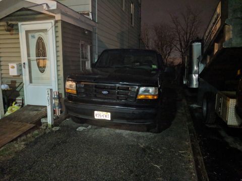 1995 Ford Bronco - This black Ford Bronco is parked in a driveway next to a house and a trailer.