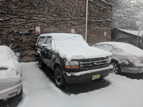 1995 Ford Bronco - A black Ford Bronco sits covered in snow, parked beside another vehicle on a winter day.