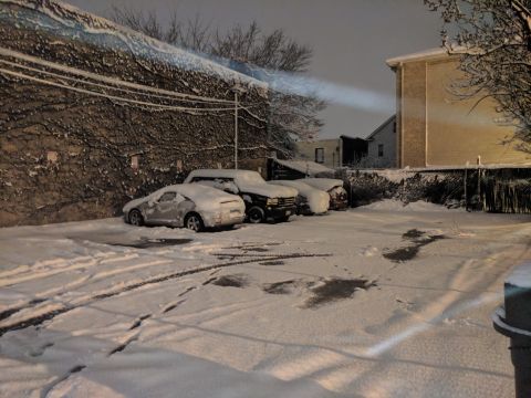 1995 Ford Bronco - A winter scene shows multiple vehicles parked in a lot, blanketed in snow with tire tracks marking the ground.