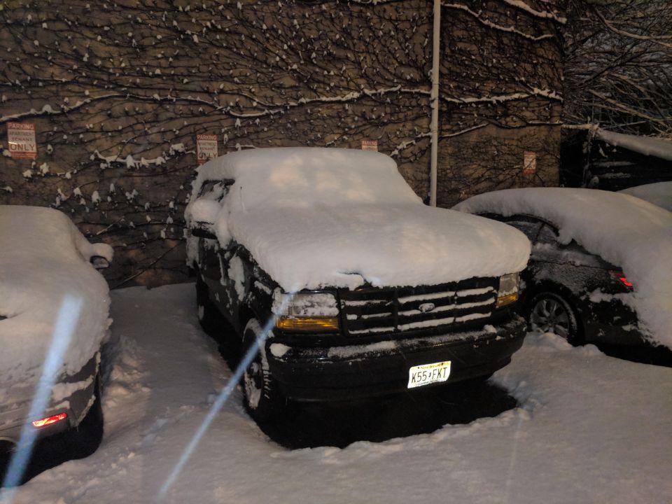 Black Ford Bronco covered in snow, parked next to another snow-covered car