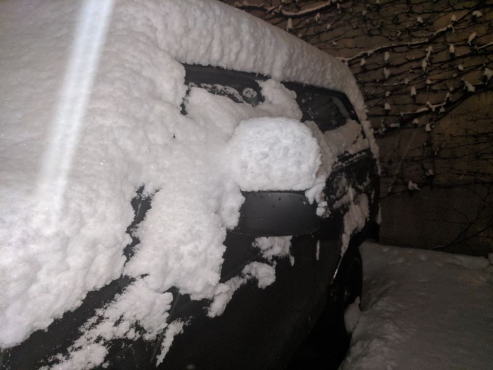 Dark colored vehicle side covered in thick snow, with a snowball on the side mirror