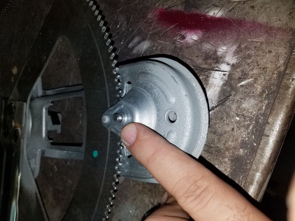 Close-up of a flywheel and starter gear mechanism with a finger pointing to a component