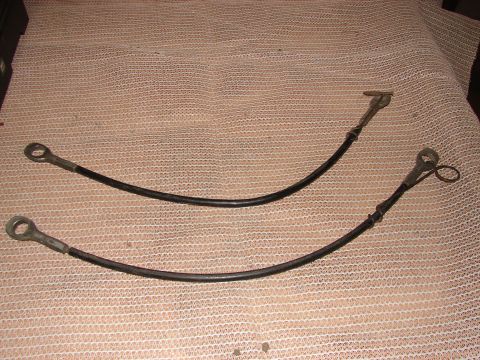 1973 Ford Ranchero - Two flexible brake cables with metal eyelet connectors are laid out on a textured surface.
