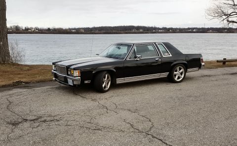 1985 Mercury Grand Marquis - A classic black Mercury Grand Marquis sits by the water on an overcast day.