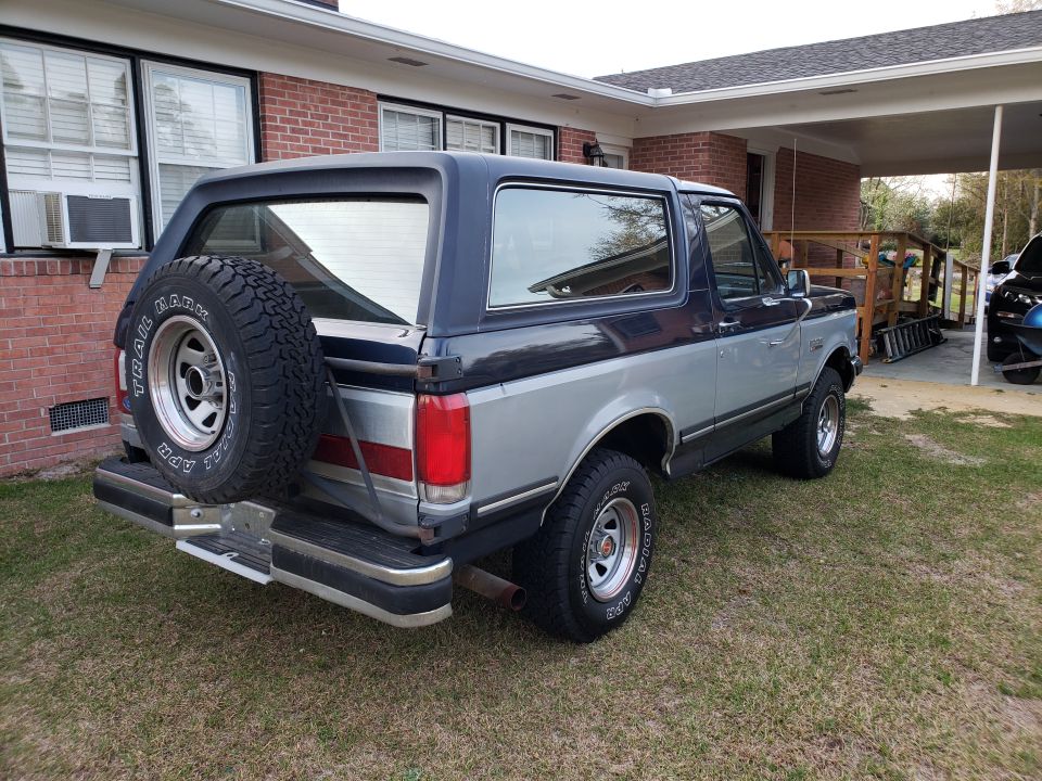 1989 Ford Bronco parked in a grassy yard next to a brick house