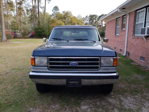 1989 Ford Bronco - Front view of a blue 1989 Ford Bronco parked in a grassy yard next to a brick house.