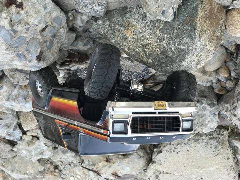 1995 Ford Bronco - This toy RC car is stuck on its side in a rocky area. The license plate is visible.