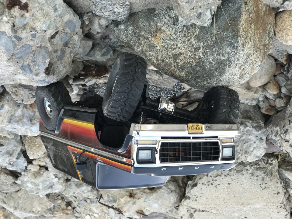 toy RC car flipped on its side among rocks. License plate reads 'FREWHEELN'