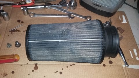 2000 Pontiac Grand Prix - A dirty air filter sits on a cardboard surface next to various tools, with a Lasko fan visible in the background.