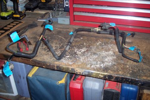 1995 Ford Bronco - A disassembled engine wiring harness lies on a cluttered workbench with tools and storage bins in the background.