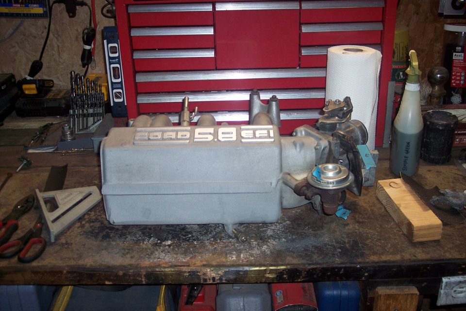 Ford 5.8 EFI intake manifold on a workbench with tools and a paper towel roll