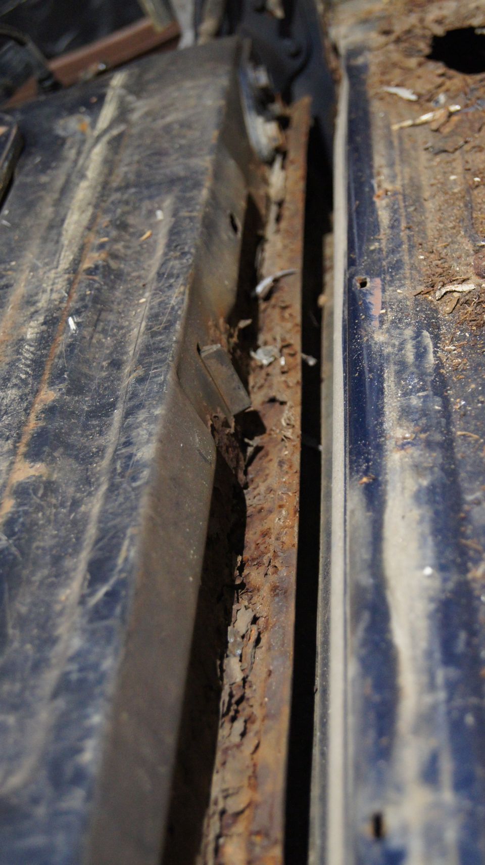 rusted out section of a vehicle's floor pan, showing significant corrosion