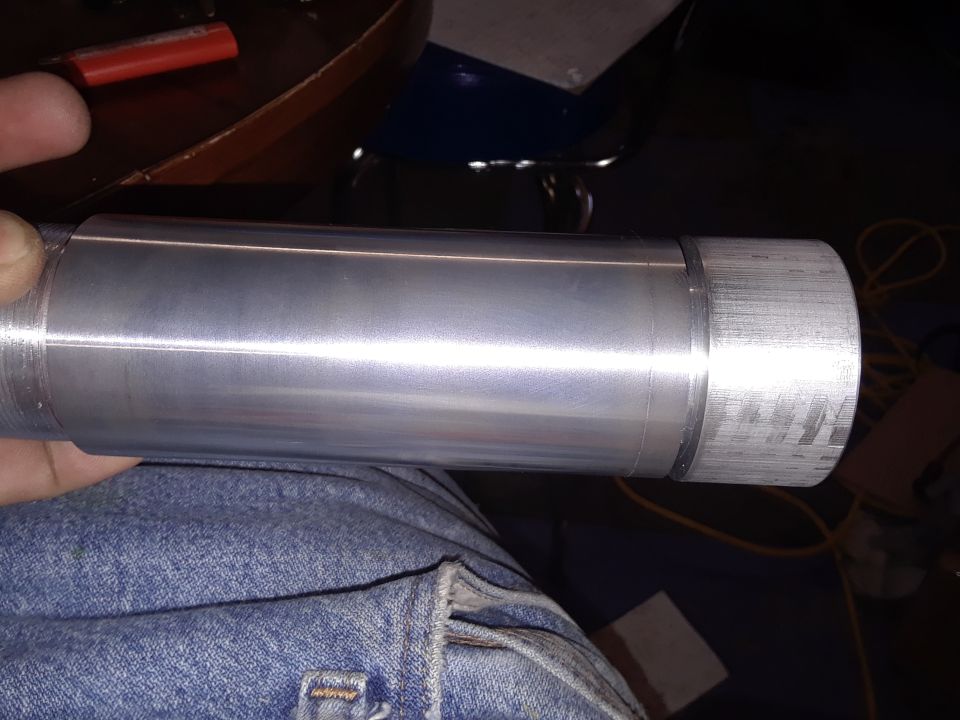 Machined aluminum cylinder with knurled end, held by a hand in jeans