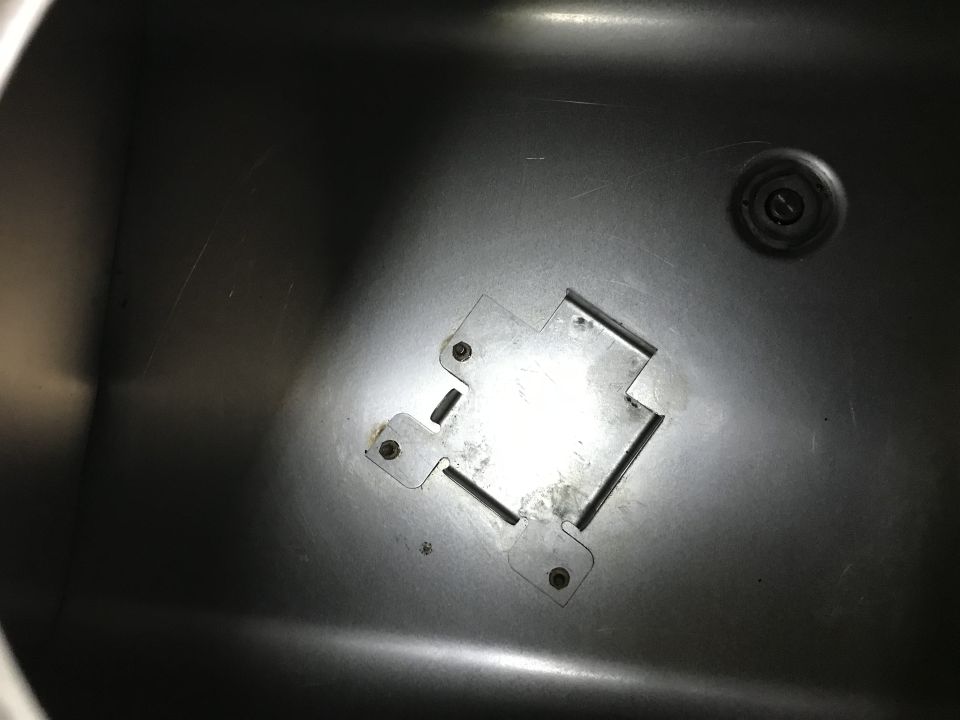 Metal sink basin with a square mounting bracket attached by four screws. A drain is visible to the right
